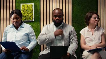 multietnisk jobb sökande väntar i de korridor med deras CV filer, framställning för formell intervju med de hr. sökande reflekterande otålighet och förtroende under huvud jakt. kamera a. video