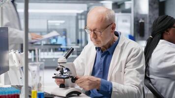 maschio ricercatore a microscopio analisi bioscienza campioni a partire dal laboratorio vassoio. messa a fuoco su cellulare osservazione e dettagliato molecolare studia sottolinea il scientifico metodo, biochimica e dati analisi. telecamera b. video