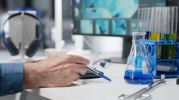 Older scientist in modern lab playing with a pen while waiting for experiment data, reflecting impatience and anxious concentration during advanced medical research in biotechnology. Camera B. video