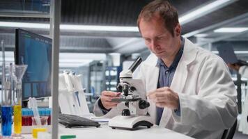 anställd studerar prov bricka under de mikroskop för forskning studie i en labb, glidning de cellulär undersökning och stödjande genetik forskning. Avancerad analys för sjukvård. kamera a. video