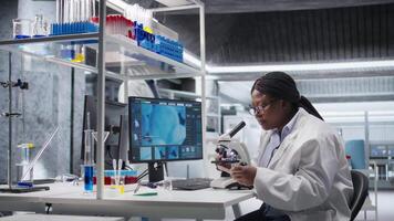forskare analyserar prover i laboratorium miljö med mikroskop och kemikalier. kvinna expert- framåt genetik forskning, kombinerande laboratorium analys med biokemi studier. kamera a. video