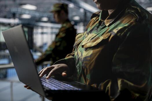 Close up of server hub employee in soldier uniform typing on laptop, running diagnostics on government systems. Army information technology specialist in data center writing code on notebook keyboard photo
