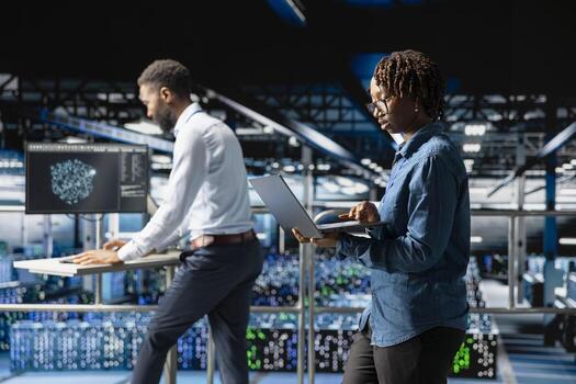 African american woman technician looking at code debugging tools on laptop, programming machine learning script for automation and innovation in data center. Server farm engineering. photo