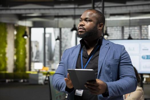 African american businessman overseeing analytics tasks with a tablet, using data and KPI metrics for business management and global expansion. Improve efficiency and productivity. photo