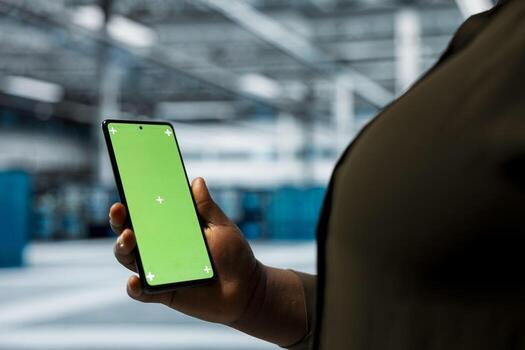 Close up of data center manager using green screen smartphone to optimize network hardware, planning capacity. Worker manages server hub resources with chroma key mobile phone for improved reliability photo