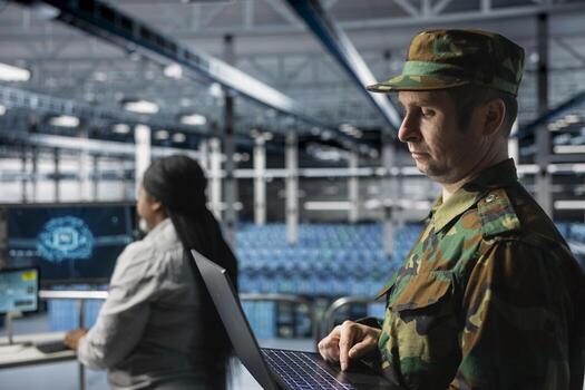 Military officer reviewing mission critical data on laptop in server room command center. Soldier wearing uniform analyzing satellite communications on notebook in army data center photo