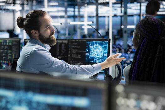 Team leader guiding intern in server room to review infrastructure diagnostics. IT specialist and african american woman in data center analyzing performance data to maintain system uptime photo