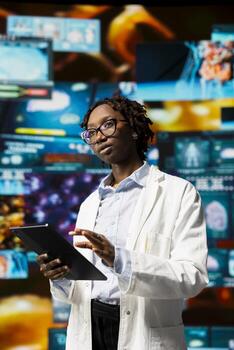 Healthcare professional using device, reviewing CT scans and MRI data analytics displayed on videowall. Scientist in medical research lab visualizing health data on futuristic panels using tablet app photo