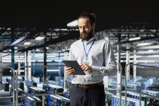 System administrator on data center industrial platform checking code on tablet, managing software updates for server rigs configuration. Male IT professional ensuring data management. photo
