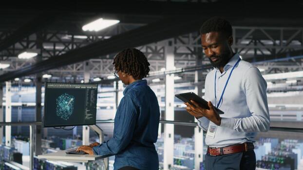 Technician walks in data center, doing maintenance tasks on tablet, ensuring optimal performance. IT expert reviewing diagnostics and applying patches to server hub gear, improving stability photo