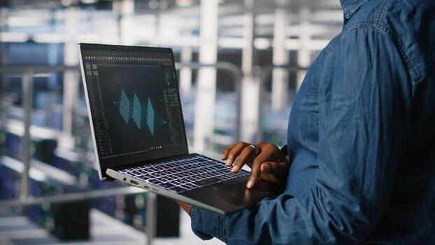 Close up of admin in data center using laptop to monitor neural network LLM visualization. Server hub IT expert overseeing rigs powering machine learning processes using notebook photo
