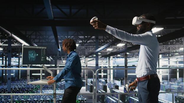 Engineer using VR headset in data center to update server tech, configuring equipment using software tools. Server hub employee reviewing hardware analytics using virtual reality, photo