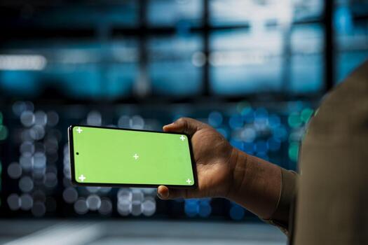 Close up of data center technician using isolated screen smartphone to monitor of network performance and system operations. Server farm worker checks equipment functionality using chroma key phone photo