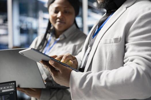 Close up of developers in data center using tablet to update infrastructure software, configuring network virtualization. Server hub IT professionals using device to verify hardware settings photo