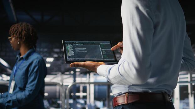 Close up of programmer swiping on tablet display in data center, doing maintenance tasks, ensuring optimal performance. IT expert checks code on device, applying patches to improve stability, photo