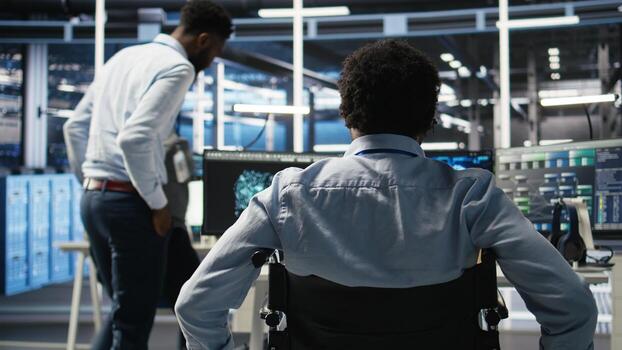 Data center programmer in wheelchair entering office uses AI node tree program to minimize system downtime. Server room IT expert in disability uses machine learning visual programming tool, camera A photo