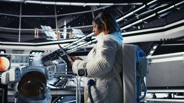 Astronaut inside high tech spacecraft checking red planet summary analytics during routine mission check. Orbit station cosmonaut using device, standing near monitor showing Mars data photo