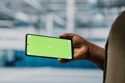 Close up of data center software developer using green screen smartphone to monitor of network performance and system operations. Server hub worker checks gear functionality using mockup mobile phone photo