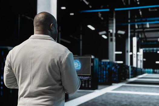 Close up of data center engineer using artificial intelligence on laptop to troubleshoot connectivity issues. Server room worker working with AI machine learning, auditing systems for vulnerabilities photo