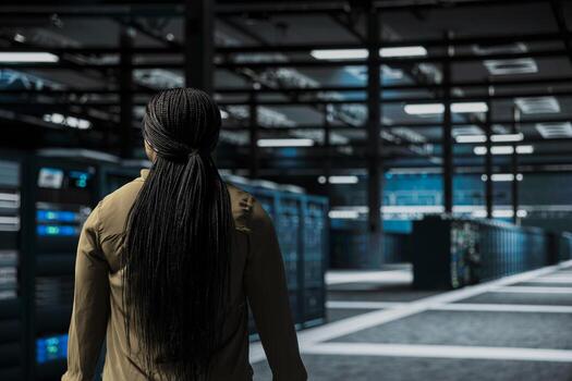 Software developer walking through server room rows lined with storage infrastructure rigs. IT worker inspecting high tech data center helping power internet services for business clients photo