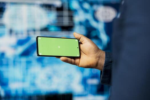 Black IT technician shows smartphone with chroma key screen, examining predictive analytics and neural networks for data processing automation and high tech innovation. Cybernetics. photo
