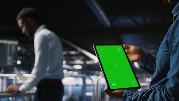 Data center engineers monitoring neural network LLM visualization using green screen tablet. Server farm IT experts oversee rigs powering machine learning processes using chroma key device, photo