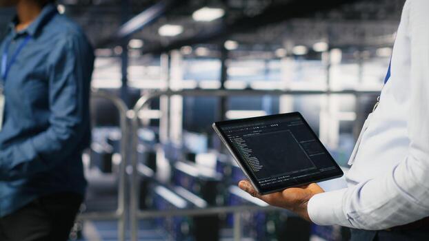 Close up of data center admin using tablet to reviewing machine learning code dashboards. Server farm IT expert using device to monitor AI infrastructure performance photo