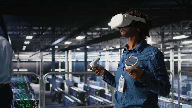 Data center programmer using virtual reality technology to simulate artificial intelligence neural networks. Woman in server farm using VR headset equipment to oversee AI systems, photo
