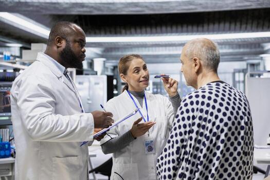 Diverse team of doctors examining a senior man for a new drug testing study, monitoring symptoms or potential allergic reactions. Looking for side effects under observation in lab. photo