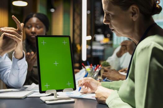Diverse project staff working at night in office with chroma key on tablet, collaborating on budgeting, reporting and setting business goals during a night meeting at a multinational company. photo