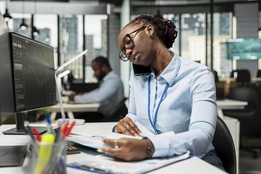 Trader discusses market trends over phone call with investing partners in prop firm office. Brokerage company employee making trading decisions while talking on smartphone at desk photo