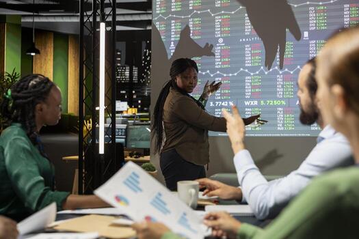 Team leader presenting data forecasting trends on projection board, shares infographics data with colleagues in a night time meeting. Corporate event to plan project development. photo