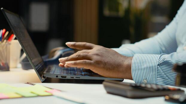 Close up of black worker proofreading and fact checking financial data, reviewing archived files after hours in strategy room. Evaluating reports, researching and organizing agenda. photo