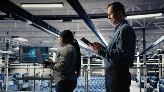 IT expert in server hub uses tablet to optimize deep learning AI systems handling tasks. Data center programmer adjusts artificial intelligence model parameters using device, camera A photo