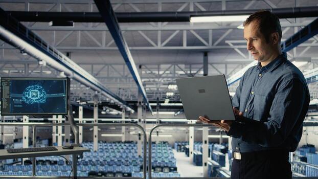 Data center IT professional deploys deep learning software on infrastructure racks. Server farm engineer trains AI systems with datasets using laptop to support applications, camera A photo