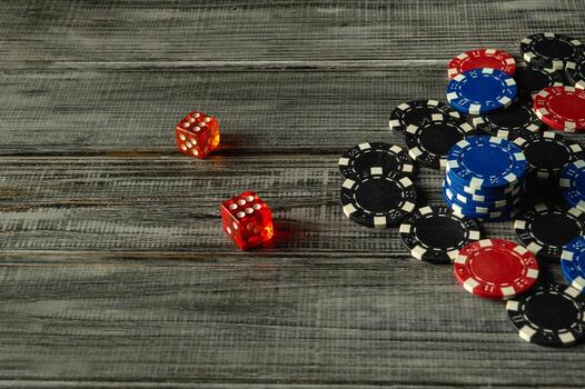 A group of poker chips in various colors stacks alongside two red dice on a rustic wooden surface, creating a vibrant and inviting atmosphere for casual tabletop gaming Craps photo