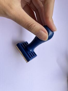 Blue Rubber Stamp Held by Hand Over White Surface with Clear Background and Simple Design Elements photo