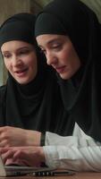 dois muçulmano o negócio mulheres dentro hijab meninas fêmea colegas de trabalho juntos usando computador portátil dentro escritório sorridente falando resolução conectados problema mulheres de negócios discutindo computador tecnologia estagiário menina com líder mulher video