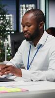 vertical africano americano empleado escritura crecimiento estrategia notas en un libro de texto, trabajando a noche con perspectivas y financiero datos. consultor asegurando Operacional éxito y eficiencia. cámara b. video