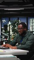 Vertical African american advisor focusing on a complex problem in a dark office at night, strategizing and envisioning options on desktop. Seeking a logical solution through careful deduction. Camera A. video