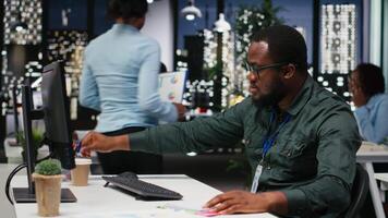 African american advisor extracting data by hand on a notebook late at night, drafting highlights from finance reports for the business administration. Notetaking supports goal setting. Camera B. video