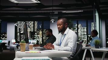 africano americano masculino trabajador corrección de pruebas financiero números, revisando archivado archivos después horas en el estrategia habitación. hombre evaluando datos en informes y haciendo investigación. cámara una. video