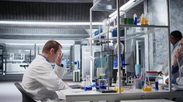 Dissatisfied scientist struggles to figure out complicated experiment data in laboratory. Confused and unsuccessful man dealing with challenges of biotechnology and genetics research. Camera A. video