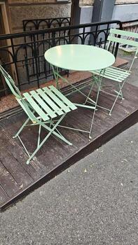 Pastel green metal chairs and table on a wooden platform outside a city building. The image suggests themes of urban leisure, simplicity and autumn solitude photo