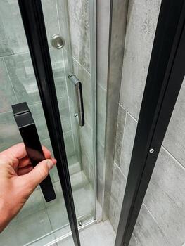 A person opens a glass shower door with a sleek black handle, adding a modern touch to the bathrooms design and functionality, while the surrounding tiles enhance the space photo