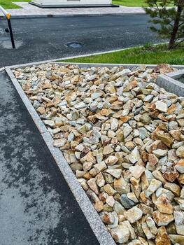 There is a sizable pile of rocks situated on the side of a road, which may include various types of stones like pebbles, rubble, and gravel that serve as building materials photo