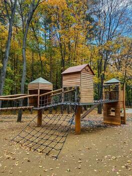 In a park, there is a beautiful wooden playground, complete with slides and swings, surrounded by lush trees that provide shade and enhance the recreational atmosphere of the area photo