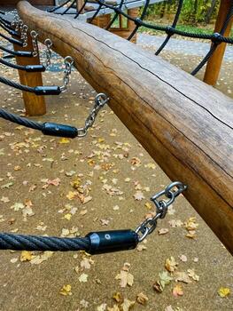 The playground has a vibrant, safe climbing structure made of sturdy wood and secure ropes, surrounded by fallen leaves in a lush setting, making it perfect for childrens exploration and play photo