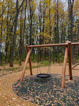 There is an empty swing set positioned right in the center of a beautiful, lush forest, surrounded by tall trees and vibrant greenery, creating a peaceful and serene play area photo