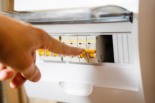 The image shows a closeup of a skilled hand adjusting switches on an electrical panel, highlighting the precise controls used by professional electrical technicians in their daily tasks photo